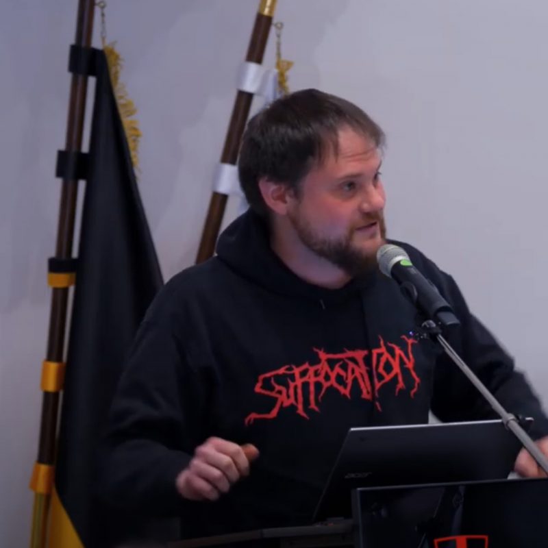 Zu sehen ist Stadtrat Markus Schillberg am Rednerpult des Gemeinderatsaals im Alten Rathaus. Im Hintergrund sind Flagge erkennbar. Die Hände hat Schillberg am Pult aufgestützt, der Blick ist ins Publikum gerichtete, während er in das Mikrofon spricht.