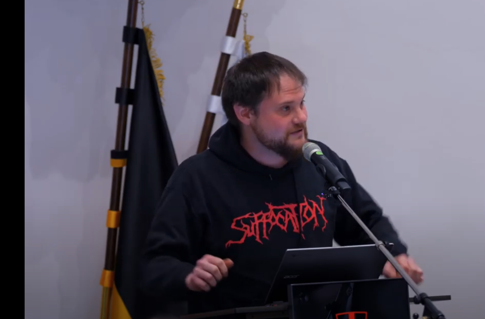 Zu sehen ist Stadtrat Markus Schillberg am Rednerpult des Gemeinderatsaals im Alten Rathaus. Im Hintergrund sind Flagge erkennbar. Die Hände hat Schillberg am Pult aufgestützt, der Blick ist ins Publikum gerichtete, während er in das Mikrofon spricht.